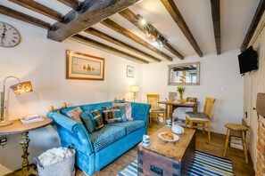 A cozy living room with a blue sofa, wooden beams, a clock, and a framed picture on the wall.