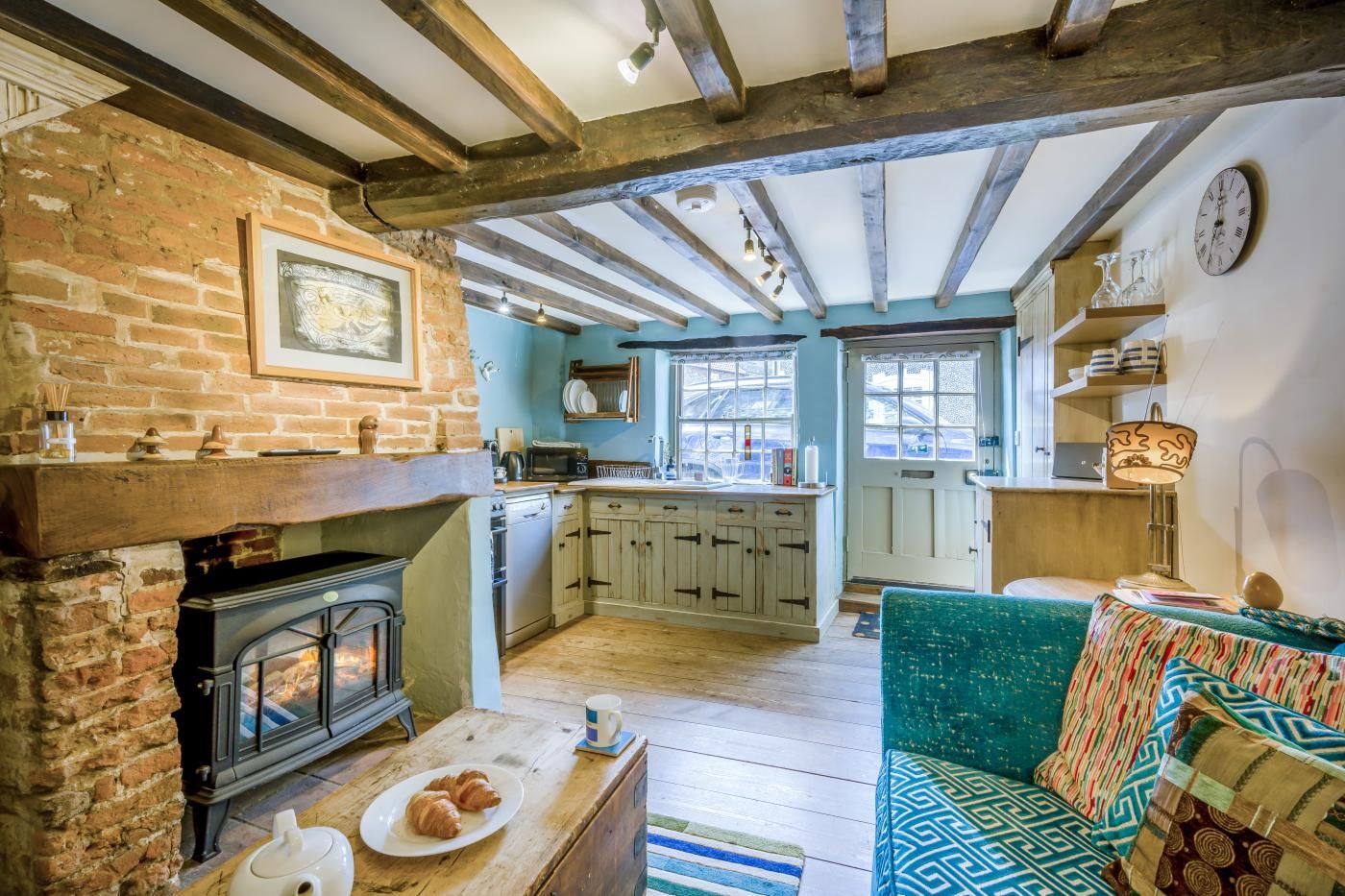 A rustic kitchen with a fireplace, wooden beams, and a view to the dining area.