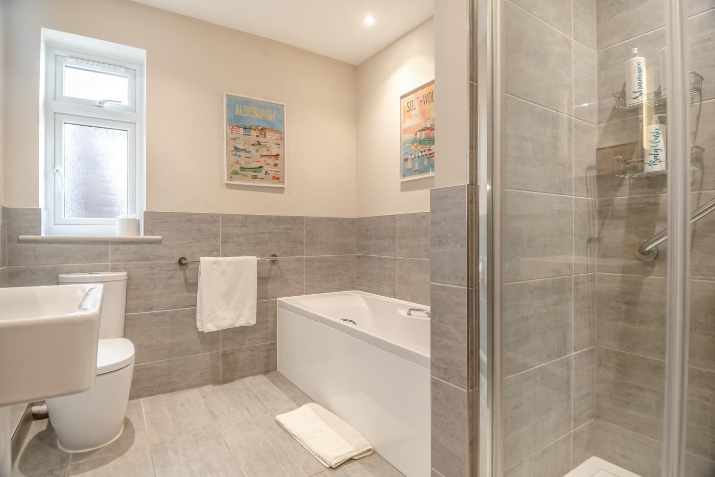 Un baño moderno con inodoro, bañera y ducha. Hay dos carteles en la pared, uno de ellos titulado 'Southwold'.