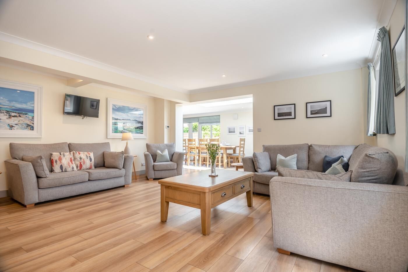 A spacious living room with two grey sofas, a wooden coffee table, and a TV mounted on the wall.