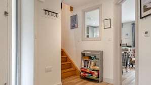 Ein Flur mit einer Holztreppe, einem Bücherregal mit Gesellschaftsspielen und einem Spiegel an der Wand.