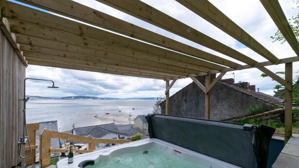 Un bain à remous sous une pergola en bois, avec vue sur la mer et la plage.