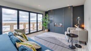 Un salon moderne avec une grande fenêtre, un canapé, une petite table avec une lampe et une cheminée.