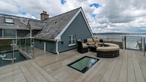Une terrasse dotée de mobilier d’extérieur, d’une balustrade en verre et offrant une vue sur la mer.