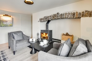 A cozy living room with a fireplace, grey sofas, and a table with cups and a kettle. - 4 Bed in Mumbles (oc-hh1222) (The Mumbles)