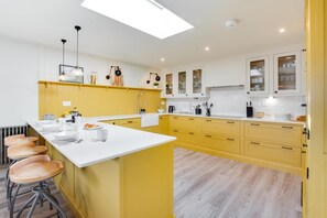 A modern kitchen with yellow cabinets, white countertops, and a central island with stools. - 4 Bed in Mumbles (oc-hh1222) (The Mumbles)