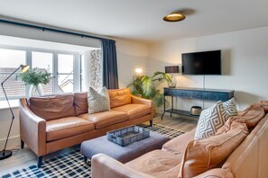A modern living room with leather sofas, a flat-screen TV, and a large window. - 4 Bed in Mumbles (oc-hh1222) (The Mumbles)