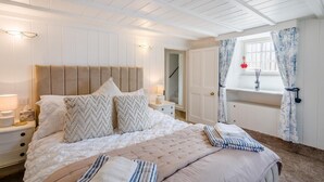 Une chambre à coucher avec un grand lit, une table de chevet, une fenêtre avec des rideaux et une porte donnant sur une autre pièce.