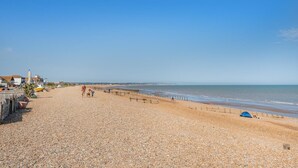 Ein Kiesstrand mit einer Holzzahlung, einem blauen Zelt und Gebäuden im Hintergrund.