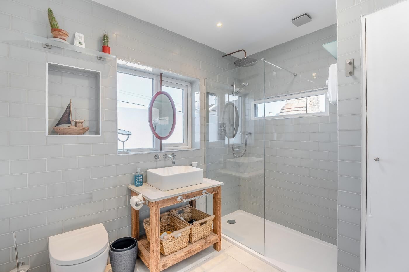 A modern bathroom with a glass-enclosed shower, a wooden vanity, and a small ship decoration on the wall.