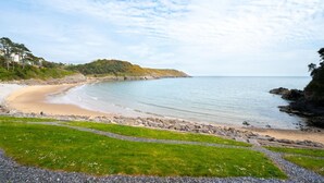 Un paisaje costero con una playa arenosa, zonas verdes y una costa rocosa.