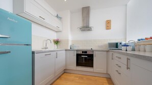 Una cocina moderna con armarios blancos, un refrigerador azul, una campana extractora de acero inoxidable y un microondas.