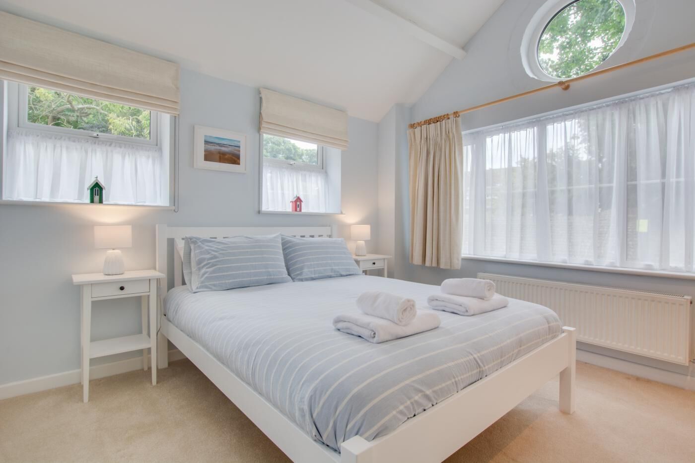 A bedroom with a large bed, two bedside tables, a window with curtains, and a radiator.