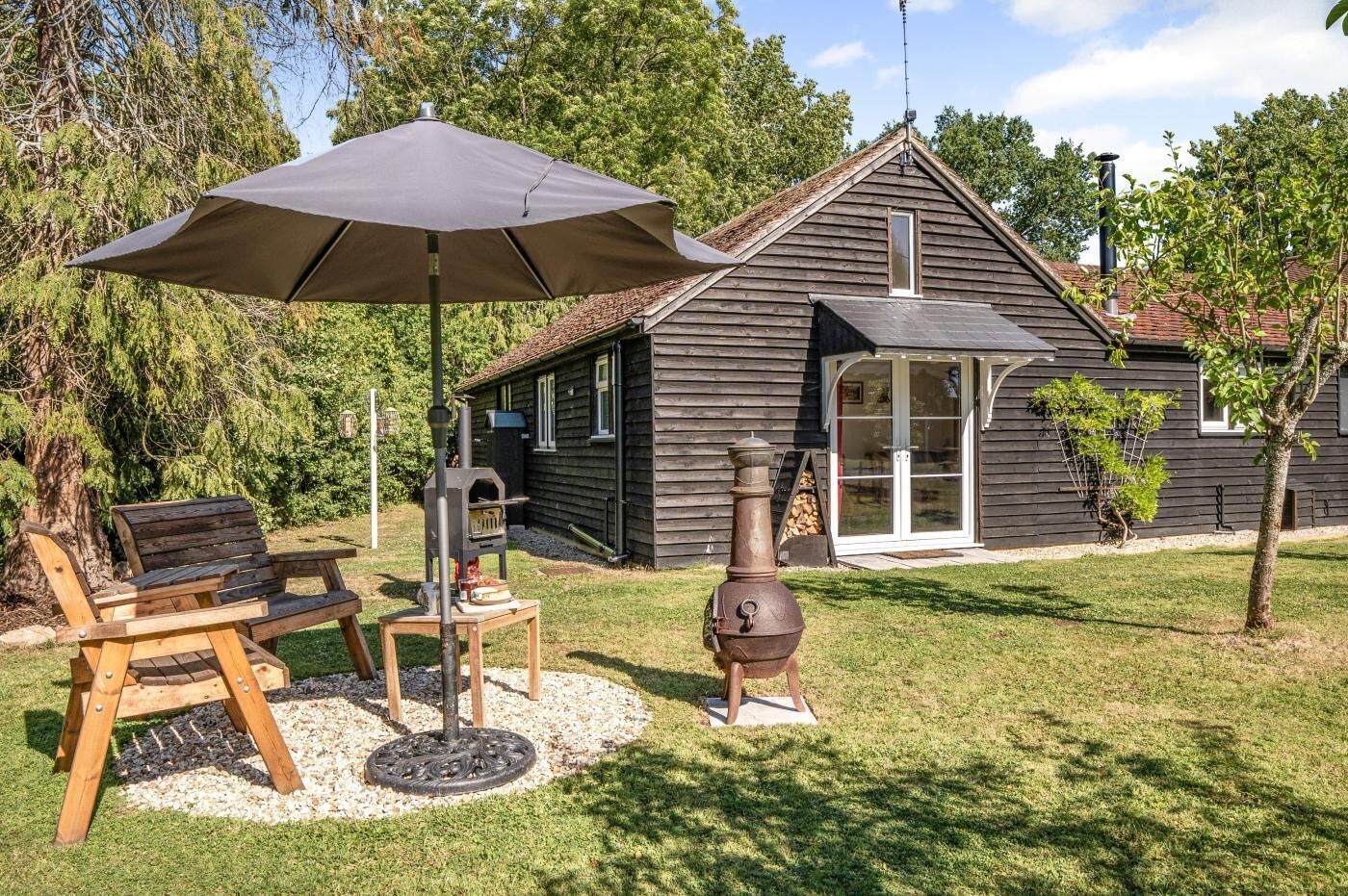 A wooden house with a chimney, a grill, and a patio with a table and chairs.