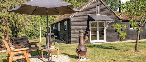 A wooden house with a chimney, a grill, and a patio with a table and chairs.