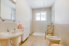 A bathroom with a bathtub, a shower, a sink, and a bidet. There is a window providing natural light and a mirror above the sink. - 1 Bed in Padstow (oc-p00485) (Saint Merryn)