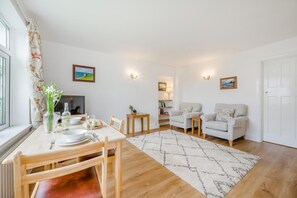 Ein gut beleuchtetes Wohnzimmer mit Essbereich, zwei Sofas, einem Couchtisch und einem Fernseher.