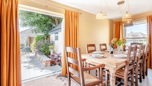 A dining area with a wooden table set for four, surrounded by chairs, with a view of a garden and a house outside. - 4 Bed in St. Peters (oc-h32665) (Broadstairs)