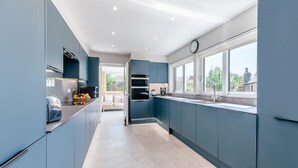 A modern kitchen with dark blue cabinets, a large window, and a view of the outdoors. - 4 Bed in St. Peters (oc-h32665) (Broadstairs)