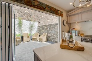 A modern kitchen with a stone wall, wicker furniture, and a wine bottle on the counter.