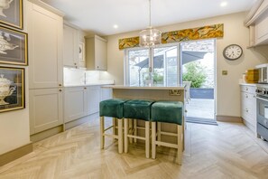 A kitchen with a central island, white cabinetry, a green bar stool, a hanging light fixture, and a clock on the wall.