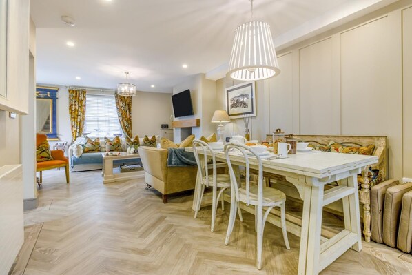 A dining area with a white table and chairs, a chandelier, and a television mounted on the wall.