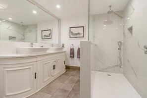 A modern bathroom with a large mirror, two sinks, a shower, and artwork on the walls.