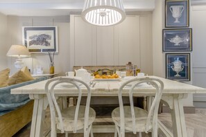 A dining area with a white table, two chairs, a chandelier, and framed artwork on the walls.