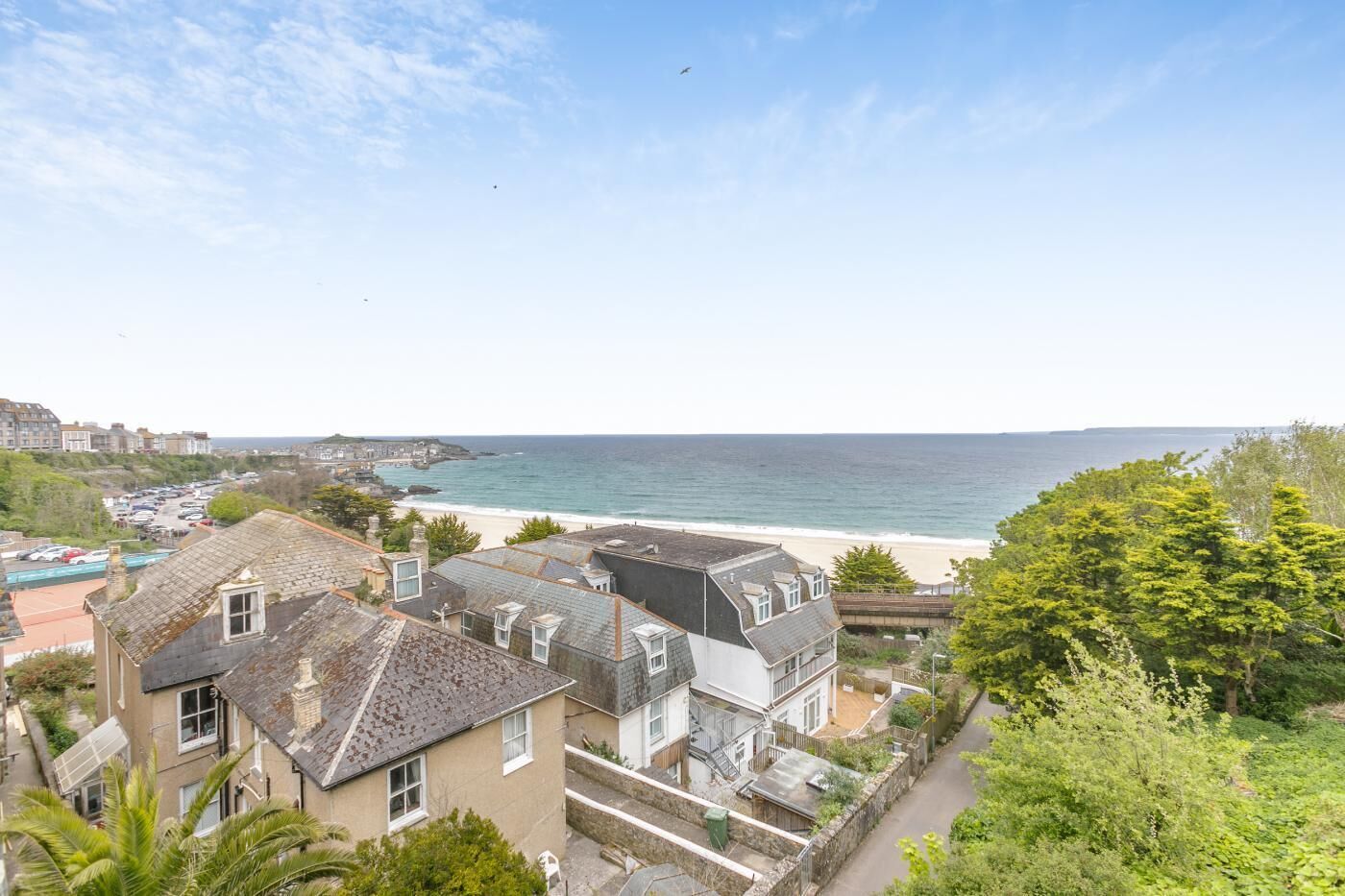 A coastal residential area with houses, a beach, and a clear sky.