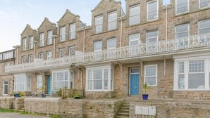 Eine Reihe von terrassenförmig angeordneten Steinwohnungen mit zahlreichen Fenstern, einem Balkon mit weißem Geländer und einer blauen Tür im Erdgeschoss.