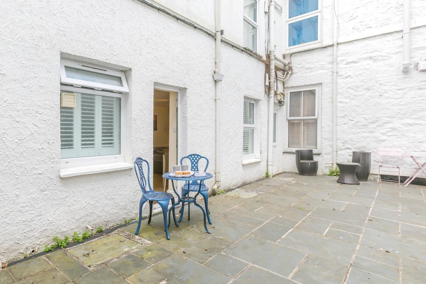 A courtyard with a white building, a table with chairs, and a trash bin.