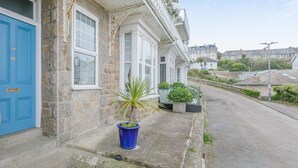 Ein Steinhaus mit einer blauen Tür, ein kleiner Garten mit einer Palme und eine Straßenansicht.