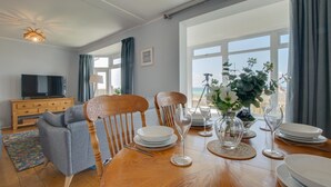 En matplats med ett träbord som är dukat för fyra personer, omgivet av stolar. En tv är monterad på ett träskåp till vänster.
