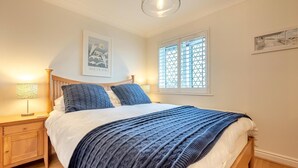 Ein Schlafzimmer mit einem Bett, einem Nachttisch, einer Lampe, einem Fenster mit Jalousien und einem Wandbild.