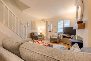 Ein Wohnzimmer mit Treppe, Fernseher, Schreibtisch und Stuhl.