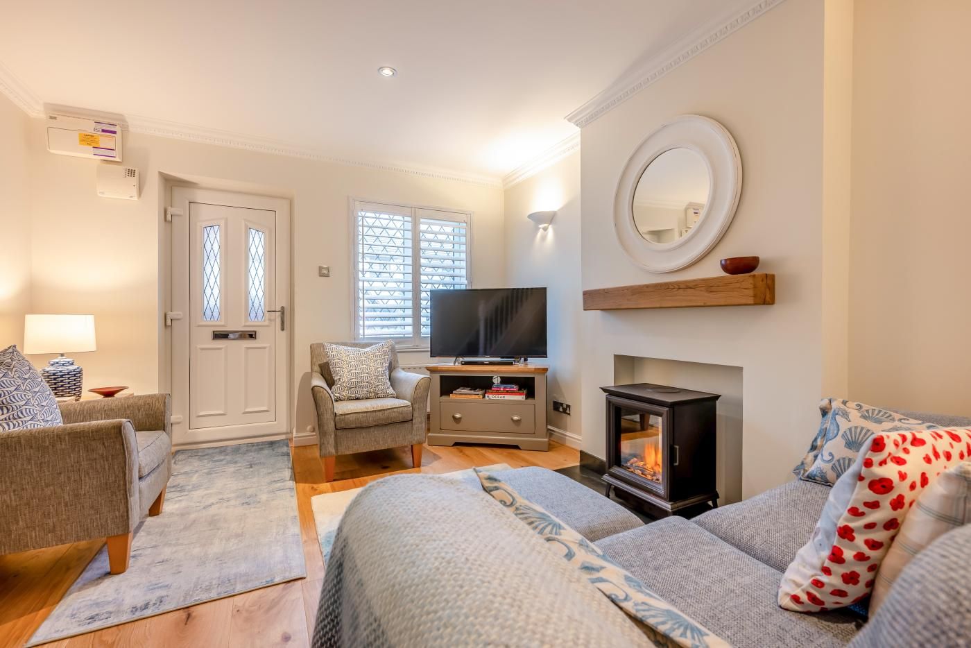 A cozy living room with a fireplace, comfortable seating, a television, and a large window with blinds.