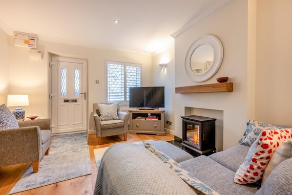 A cozy living room with a fireplace, comfortable seating, a television, and a large window with blinds. - 2 Bed in Padstow (oc-p00400) (Padstow)