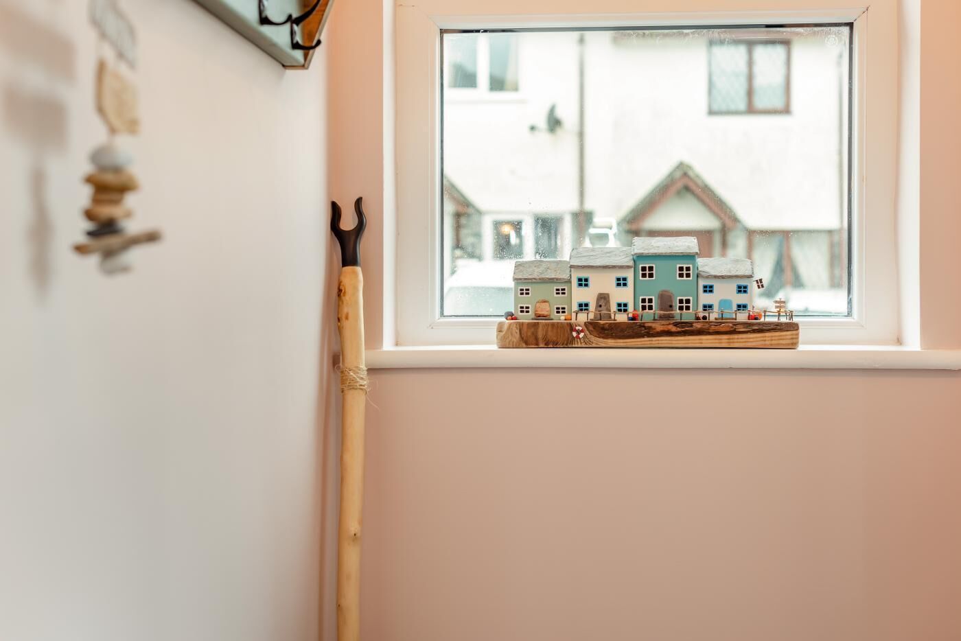 A window sill with a model train set and a wooden stick leaning against the wall.