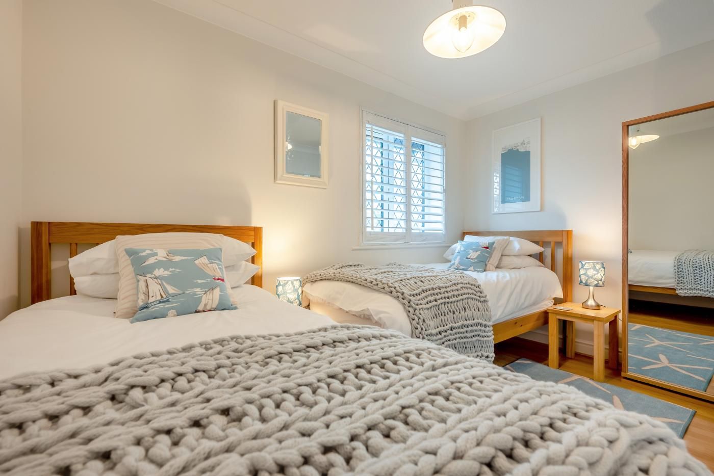 A bedroom with two beds, a large mirror, and a window with blinds.