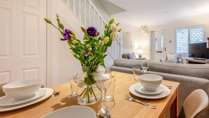 Ein Essbereich mit einem für zwei Personen gedeckten Tisch, einer Blumenvase und einem Wohnzimmer im Hintergrund.