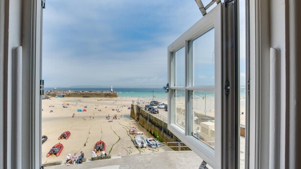 A view of a beach from a window, including the sea, beachgoers, and a lighthouse in the distance. - 2 Bed in St Ives (oc-pc055a) (St Ives)