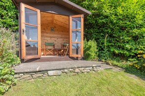 A wooden cabin with an open door, two folding chairs, and a stone wall in front. - 3 Bed in Ambleside (oc-h32727) (Ambleside)