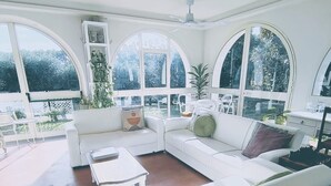 Un salon spacieux avec un canapé blanc, une table basse et une grande fenêtre en arc de cercle offrant une vue sur l’extérieur.