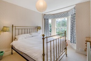 A bedroom with a four-poster bed, a window with curtains, a lamp, and a small table. - 3 Bed in Aldeburgh (oc-f32700) (Aldeburgh)