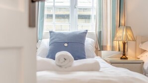 A neatly made bed with a blue pillow, a rolled white towel, and a bedside lamp on a nightstand. - 3 Bed in Padstow (oc-p00397) (Padstow)