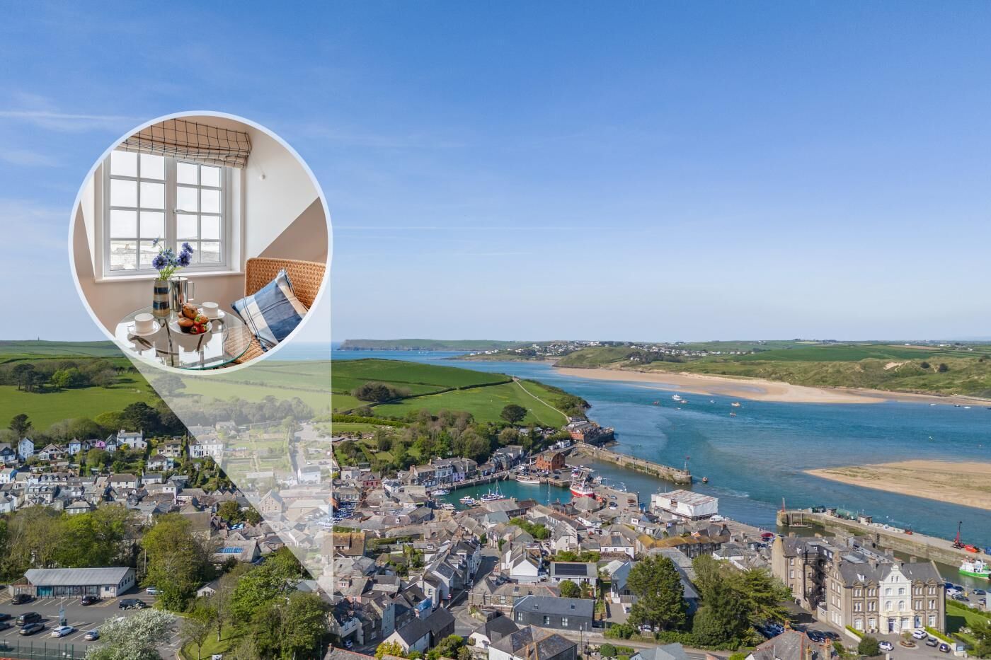 A coastal town with a view of the sea, a dock, and a circular inset of a room with a window, a table, and a chair.