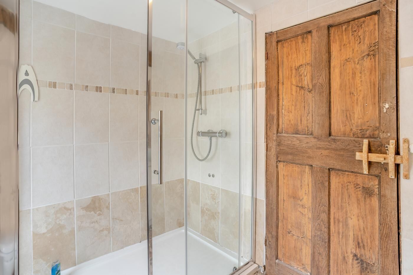 Ducha con puerta de vidrio y puerta de madera con asa metálica.