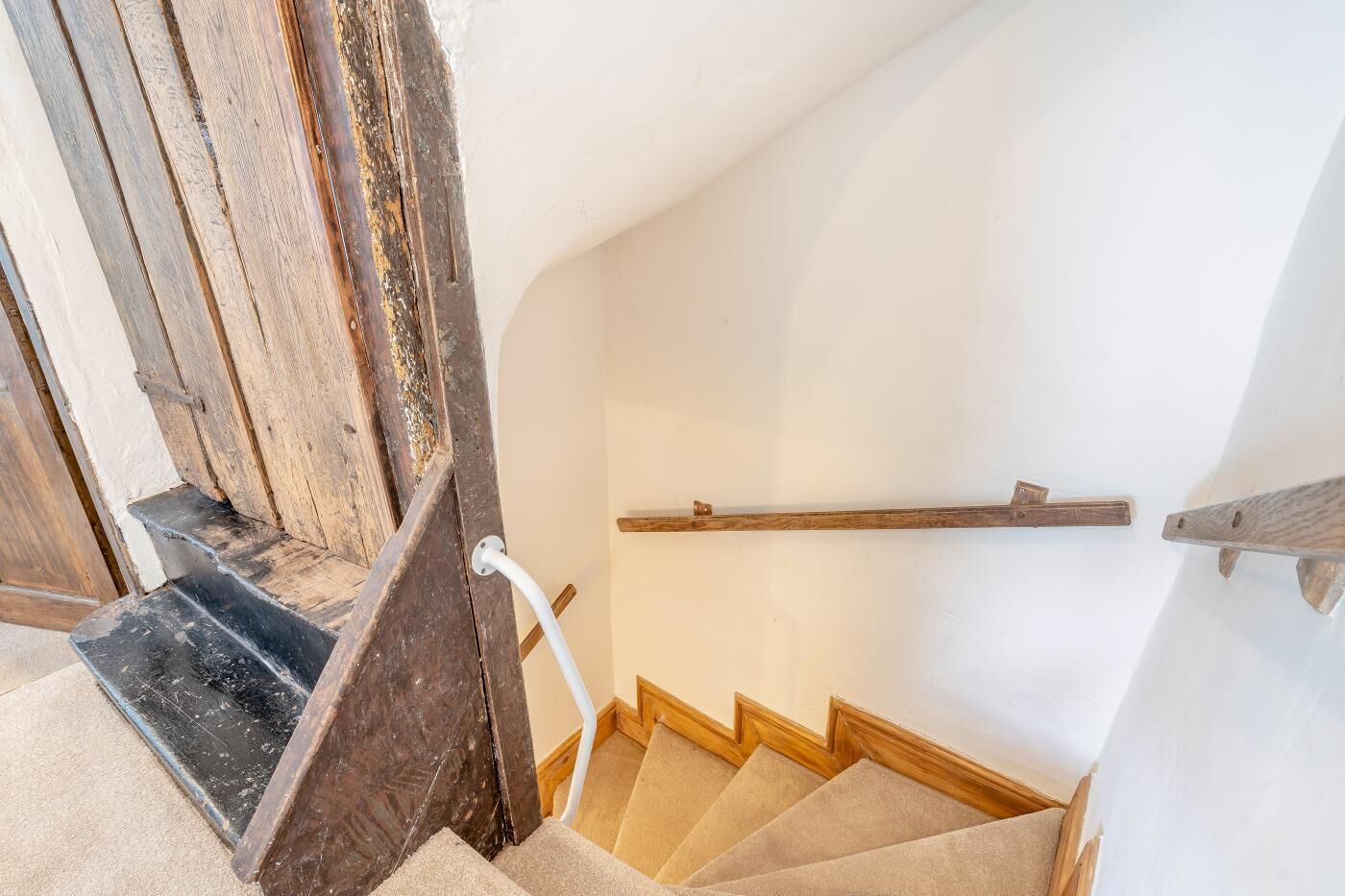 Eine Holztreppe mit Handlauf, Teppichstufen und einer weißen Wand.