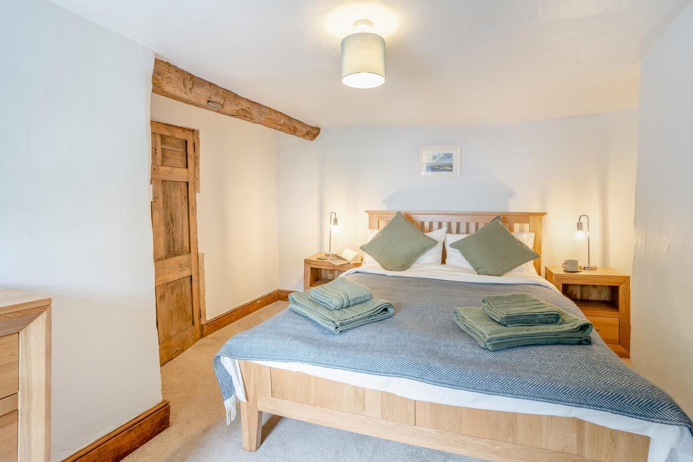 A bedroom with a wooden bed, two bedside tables, a nightstand, a wooden door, and a ceiling light fixture.