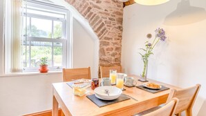Une table de petit-déjeuner dressée avec une assiette, un bol, un verre de jus d’orange, un verre de lait, une tasse, un pot de confiture et une petite plante en pot.